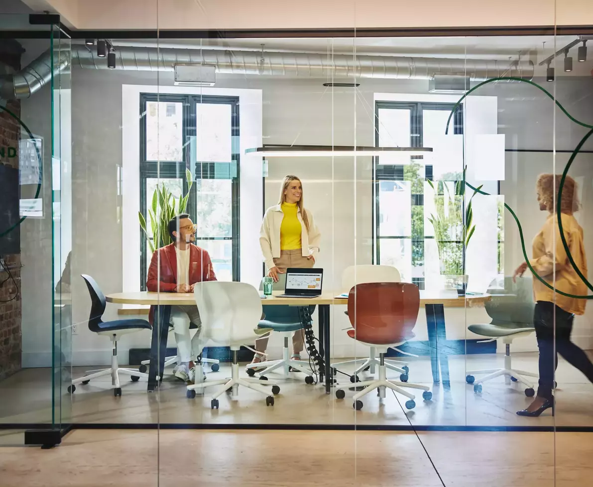 Female and male are sitting and female is standing at a table in a office meeting room